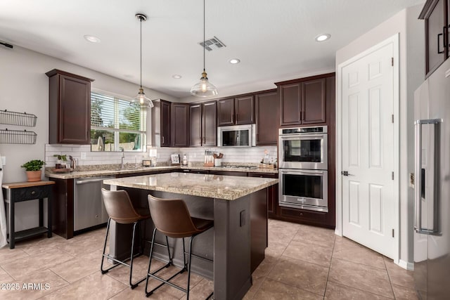 kitchen featuring dark brown cabinetry, visible vents, decorative backsplash, a kitchen island, and stainless steel appliances