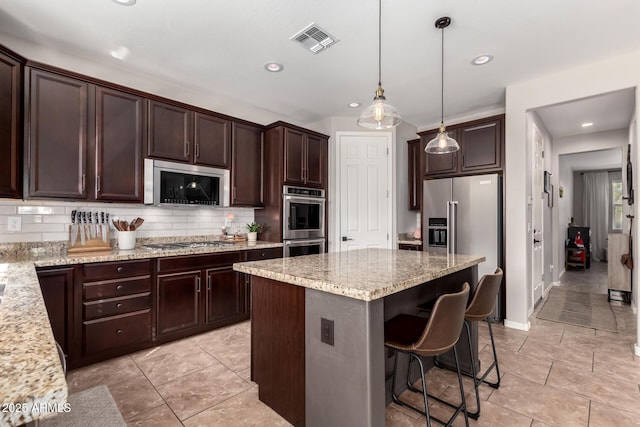 kitchen with visible vents, a kitchen breakfast bar, dark brown cabinets, appliances with stainless steel finishes, and tasteful backsplash