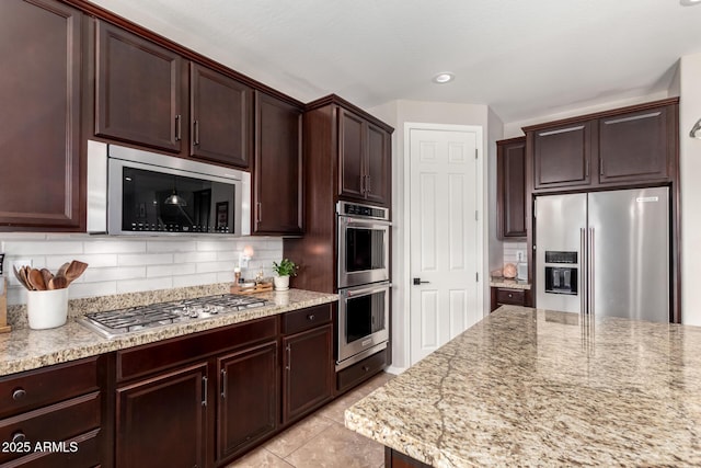 kitchen featuring light tile patterned floors, appliances with stainless steel finishes, light stone countertops, dark brown cabinets, and backsplash