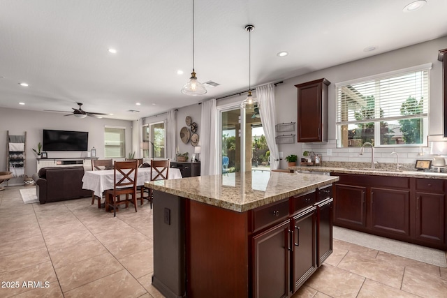 kitchen featuring decorative light fixtures, open floor plan, a kitchen island, a sink, and light stone countertops