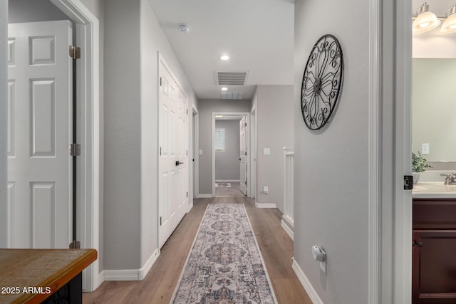 corridor featuring recessed lighting, visible vents, light wood-style floors, a sink, and baseboards