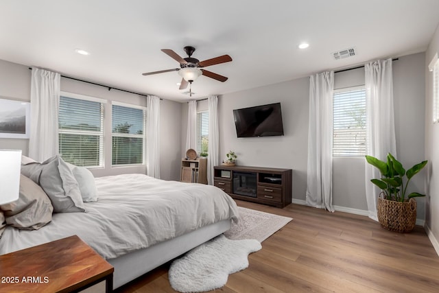 bedroom featuring baseboards, visible vents, multiple windows, and wood finished floors