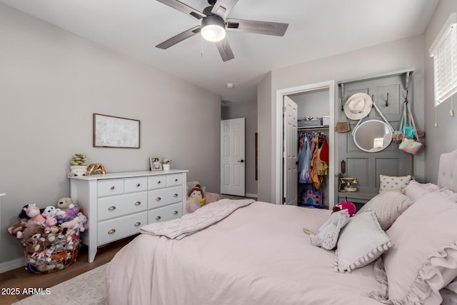 bedroom with a spacious closet, a closet, wood finished floors, and a ceiling fan