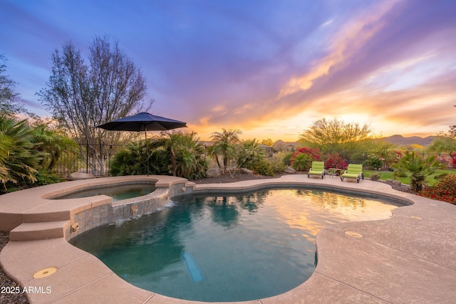 pool at dusk with a pool with connected hot tub and a patio area