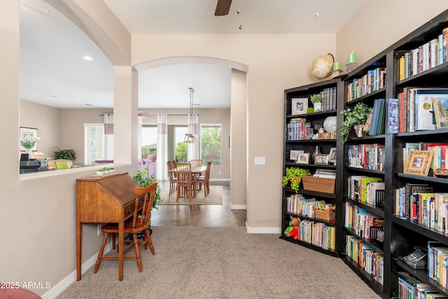 interior space featuring carpet floors, a ceiling fan, tile patterned flooring, baseboards, and arched walkways