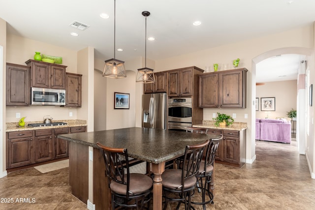 kitchen with visible vents, a kitchen island, dark brown cabinets, arched walkways, and stainless steel appliances