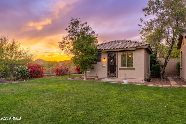view of front of property featuring a fenced backyard, stucco siding, a tiled roof, and a front yard