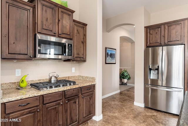 kitchen with arched walkways, baseboards, dark brown cabinetry, and stainless steel appliances
