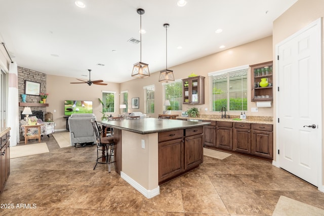 kitchen with visible vents, a stone fireplace, a breakfast bar area, a center island, and a ceiling fan