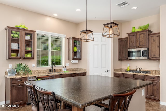 kitchen featuring visible vents, dark brown cabinetry, a sink, appliances with stainless steel finishes, and decorative light fixtures