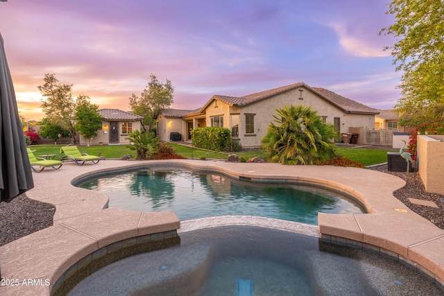 pool at dusk with a lawn, a pool with connected hot tub, and a patio area