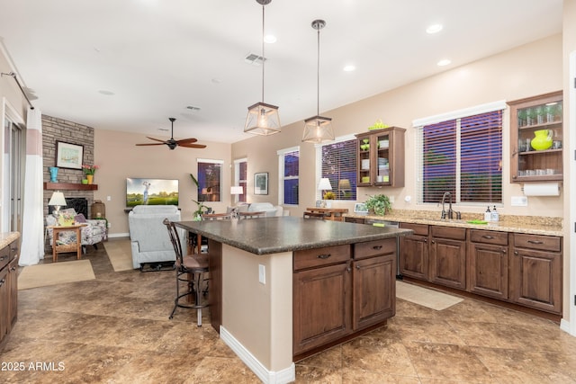 kitchen with ceiling fan, a sink, a stone fireplace, a kitchen bar, and glass insert cabinets