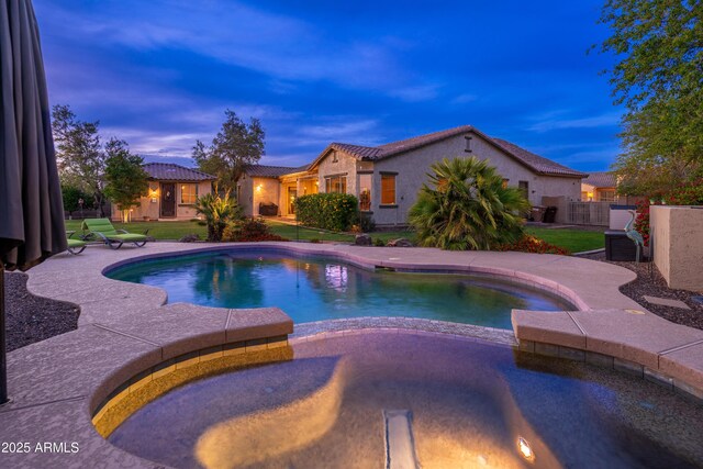 view of swimming pool featuring a lawn, a pool with connected hot tub, and fence