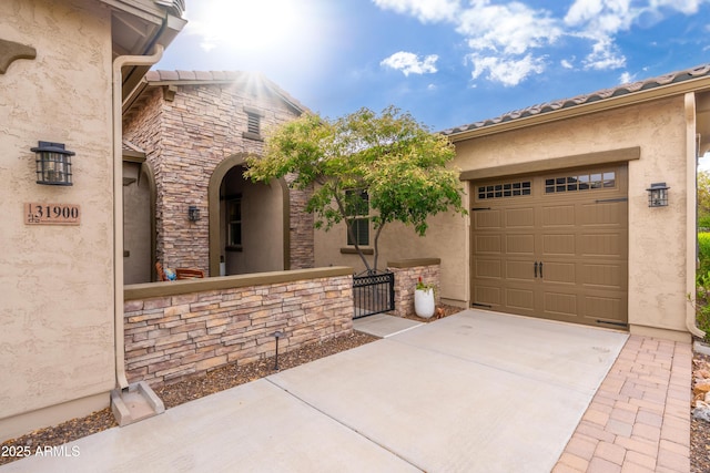 view of side of home with an attached garage, stone siding, stucco siding, a gate, and driveway