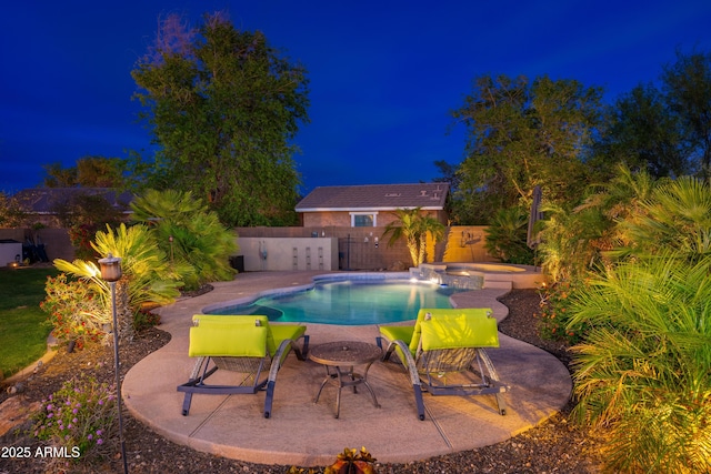 pool at night featuring a pool with connected hot tub, fence, and a patio area