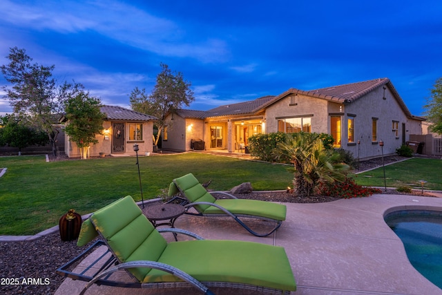 back of house at dusk with a yard, a patio, a tile roof, and stucco siding