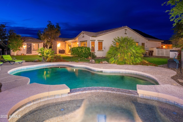 pool at night with a lawn and a pool with connected hot tub