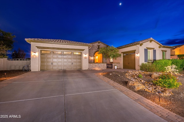 mediterranean / spanish house featuring a tile roof, concrete driveway, an attached garage, stone siding, and stucco siding