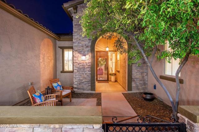 exterior entry at night featuring stone siding and stucco siding