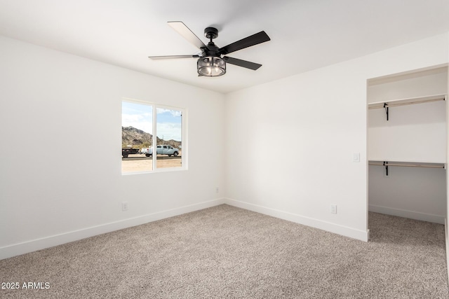 unfurnished bedroom featuring baseboards, carpet floors, a spacious closet, and a ceiling fan