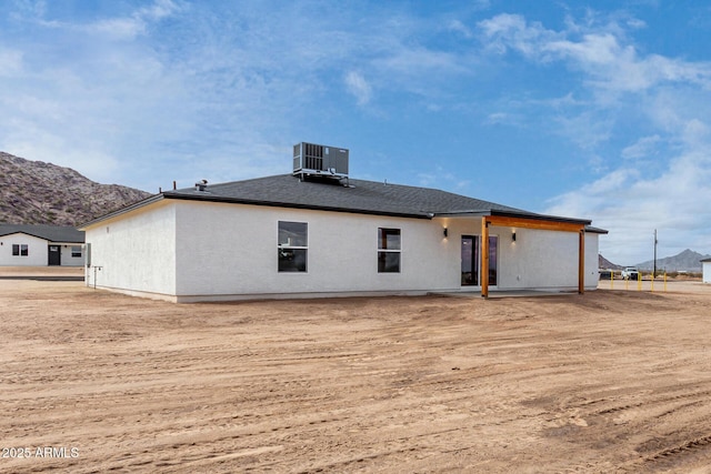 rear view of property featuring a shingled roof, central AC unit, a mountain view, and a patio area