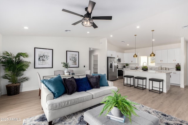 living room with a ceiling fan, lofted ceiling, light wood-style flooring, and visible vents