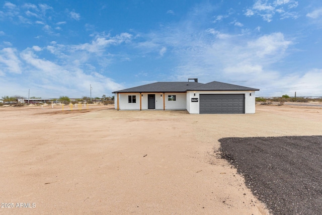 view of front of property with dirt driveway, a garage, and stucco siding