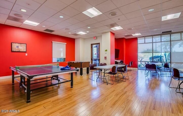 recreation room with a drop ceiling, light wood-type flooring, and a wall of windows