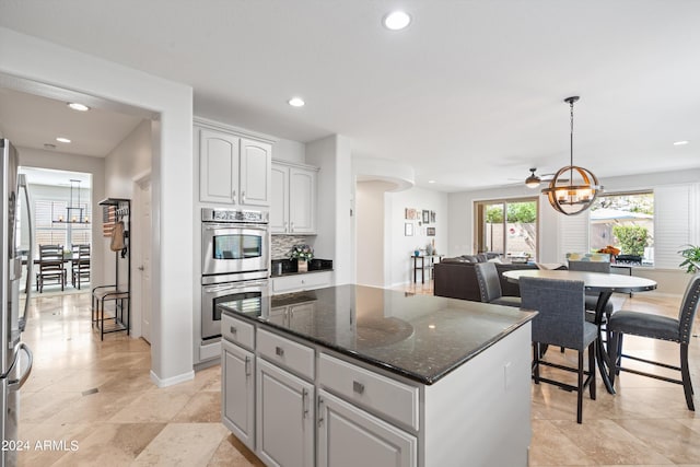 kitchen with tasteful backsplash, hanging light fixtures, double oven, a kitchen island, and dark stone counters