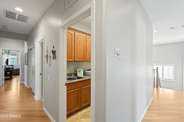 hall with baseboards, light wood-style flooring, visible vents, and a sink