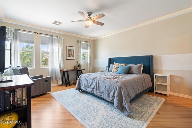 bedroom with ceiling fan, light wood-style flooring, visible vents, baseboards, and ornamental molding