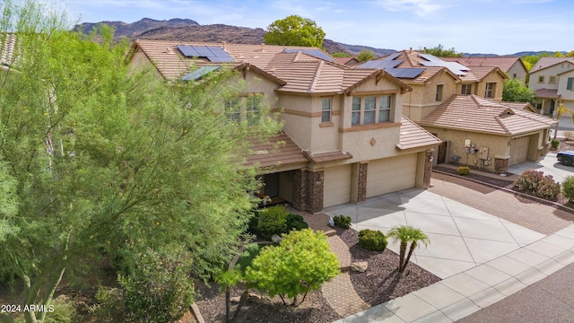 view of front facade with an attached garage, a mountain view, solar panels, concrete driveway, and stucco siding