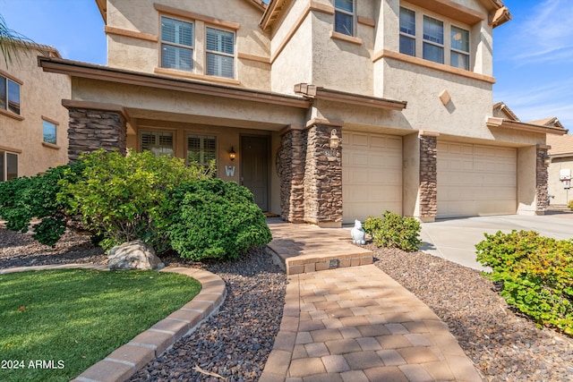 view of front of house featuring a garage, driveway, stone siding, and stucco siding