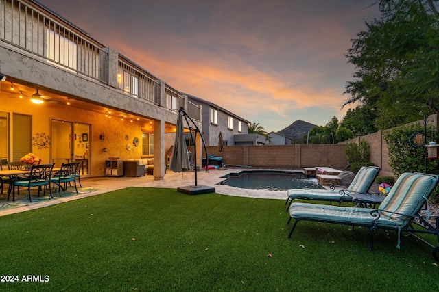 yard at dusk featuring a balcony, a fenced backyard, a fenced in pool, and a patio