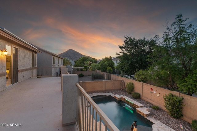 pool at dusk with a mountain view, a fenced backyard, and a fenced in pool