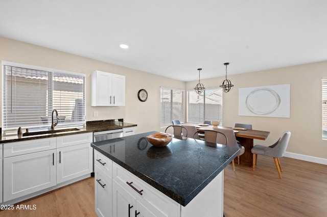 kitchen featuring a kitchen island, pendant lighting, light hardwood / wood-style flooring, dark stone countertops, and white cabinetry