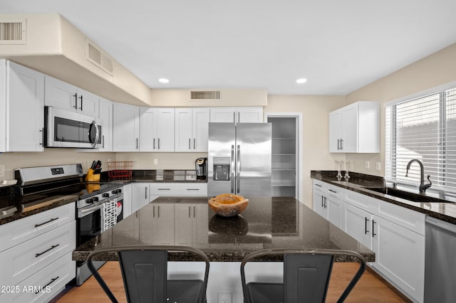 kitchen with a center island, sink, dark stone countertops, appliances with stainless steel finishes, and a breakfast bar area