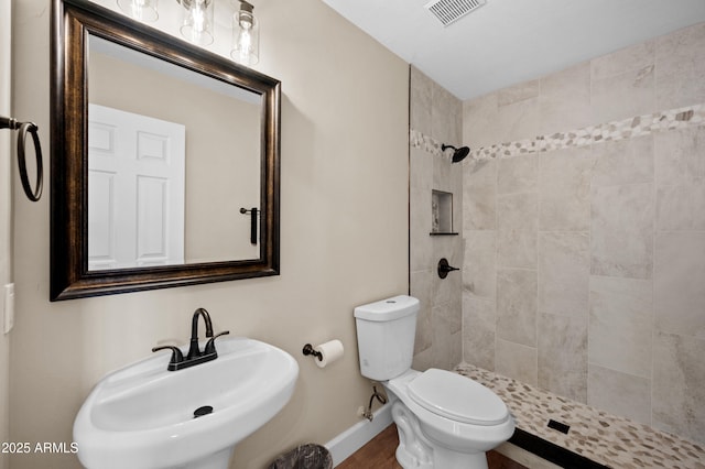 bathroom with toilet, sink, and a tile shower