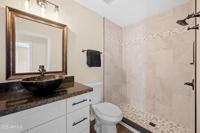 bathroom with a tile shower, vanity, and toilet