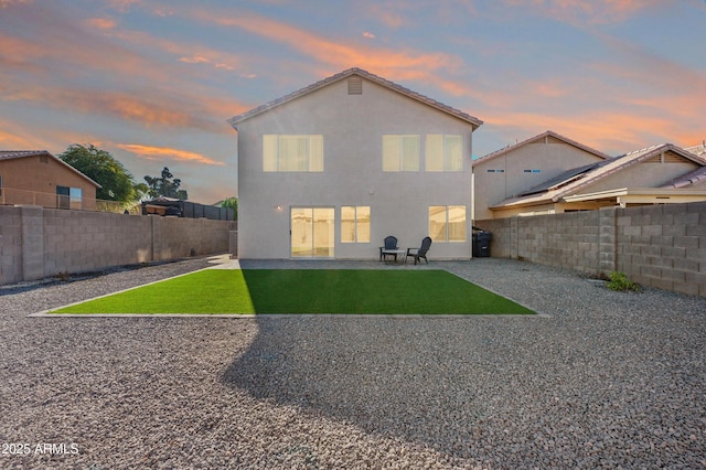 back house at dusk featuring a yard and a patio