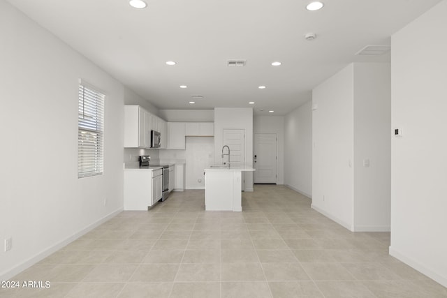 kitchen with stainless steel appliances, sink, white cabinets, an island with sink, and light tile patterned flooring