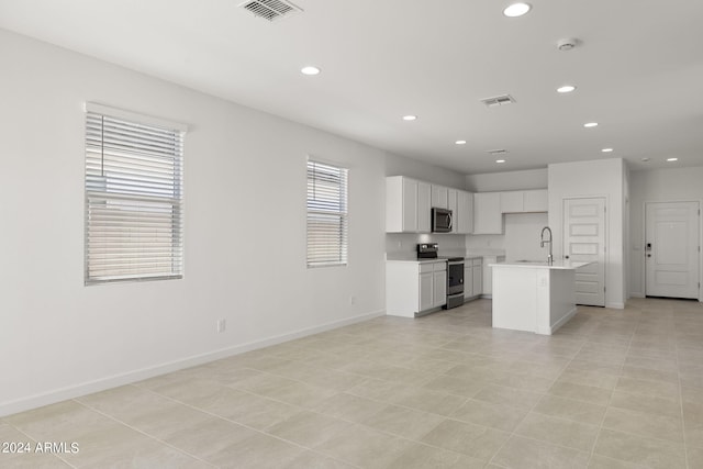 kitchen with sink, stainless steel appliances, light tile patterned floors, a kitchen island with sink, and white cabinets