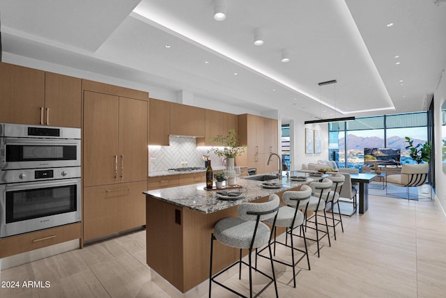 kitchen with a kitchen bar, appliances with stainless steel finishes, light stone counters, a spacious island, and sink