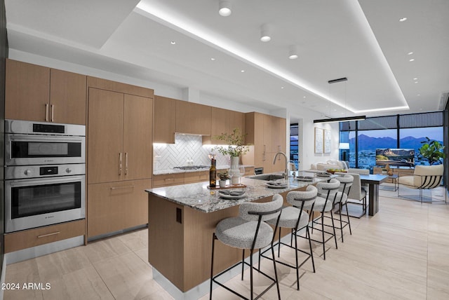 kitchen featuring a kitchen breakfast bar, sink, a large island, light stone counters, and stainless steel appliances