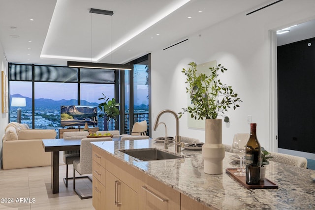 kitchen featuring light brown cabinetry, light stone counters, sink, a wall of windows, and hanging light fixtures