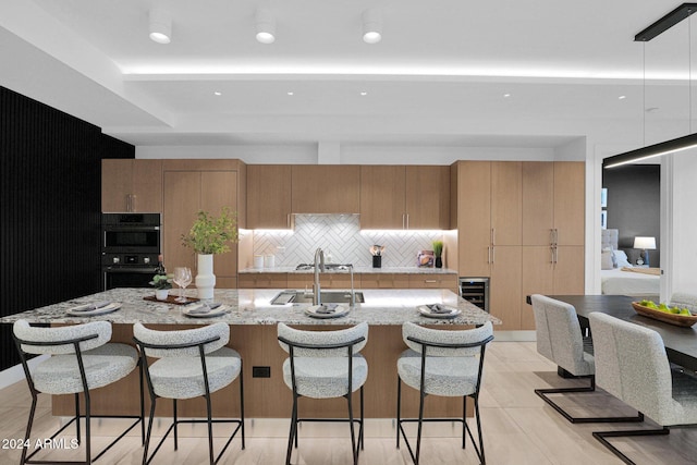 kitchen featuring a center island with sink, decorative backsplash, sink, and double oven