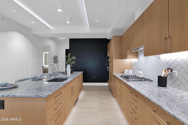 kitchen with sink, stainless steel gas cooktop, light stone counters, backsplash, and light tile patterned floors