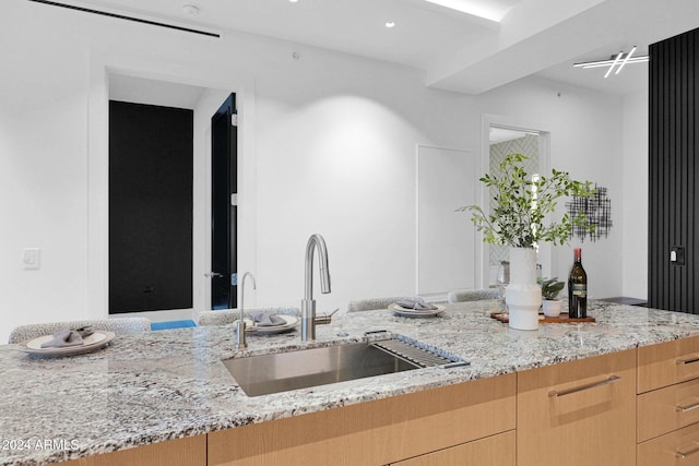 kitchen featuring light stone counters, sink, and light brown cabinets