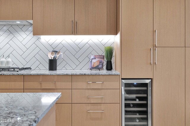 kitchen with stainless steel gas stovetop, wine cooler, decorative backsplash, light stone countertops, and light brown cabinetry