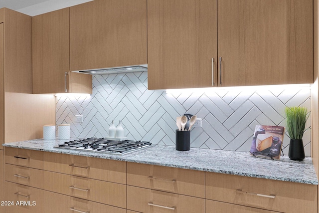 kitchen with light stone counters, extractor fan, stainless steel gas stovetop, decorative backsplash, and light brown cabinetry